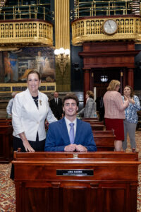 Sen. Baker joins intern Eli Peifer seated at her desk on the Senate floor.
