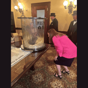 Pic 1: Sen. Baker looking at Punxsutawney Phil; Pic 2: Sen. Baker closeup shot smiling with Phil; Pic 3: Phil in glass case; Pic 4: Phil in case with arm on glass