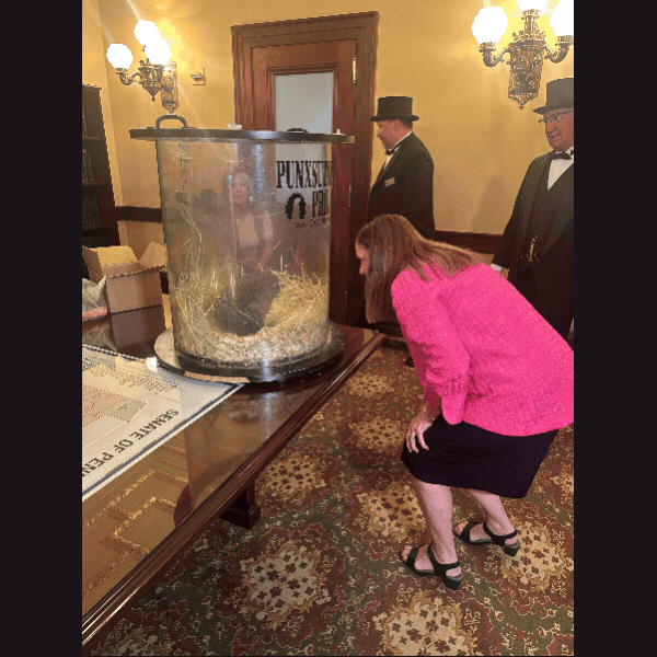 Pic 1: Sen. Baker looking at Punxsutawney Phil; Pic 2: Sen. Baker closeup shot smiling with Phil; Pic 3: Phil in glass case; Pic 4: Phil in case with arm on glass